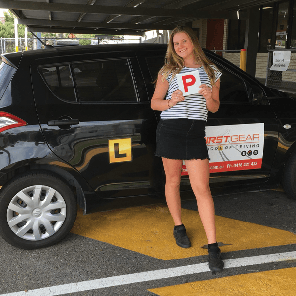 Learner driver standing next to car after a successful driving lesson holding her P plate